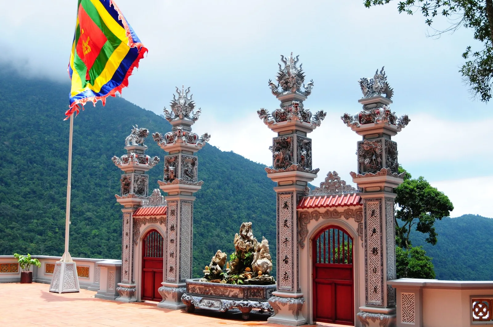 Những cột đá chạm khắc tinh xảo và cờ Phật giáo nhiều màu trước cổng đền trên núi ở Tam Đảo.